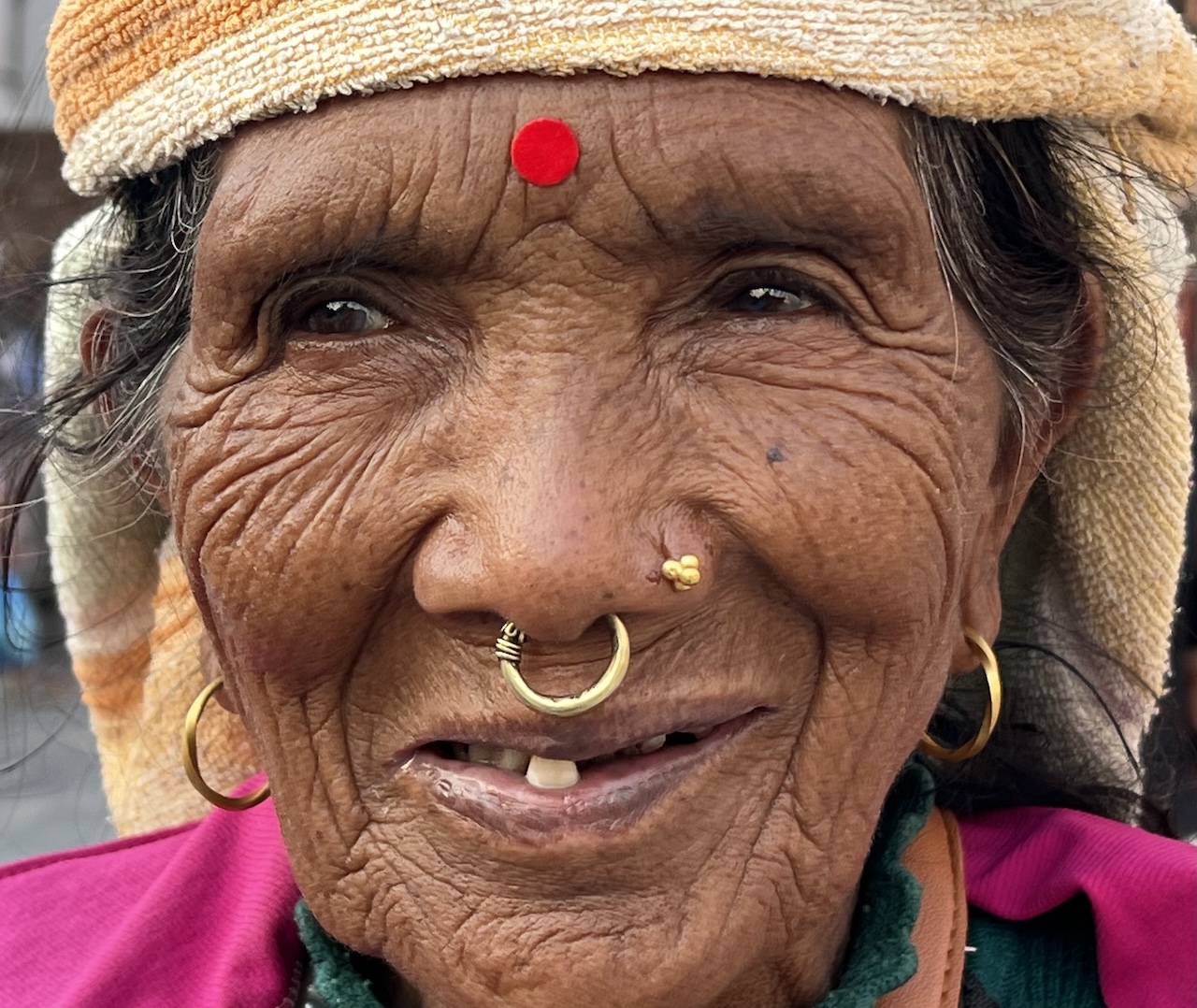 Incontro a Katmandu Primo piano di anziana sorridente con anello al naso, bindi rosso, orecchini d'oro e rughe profonde