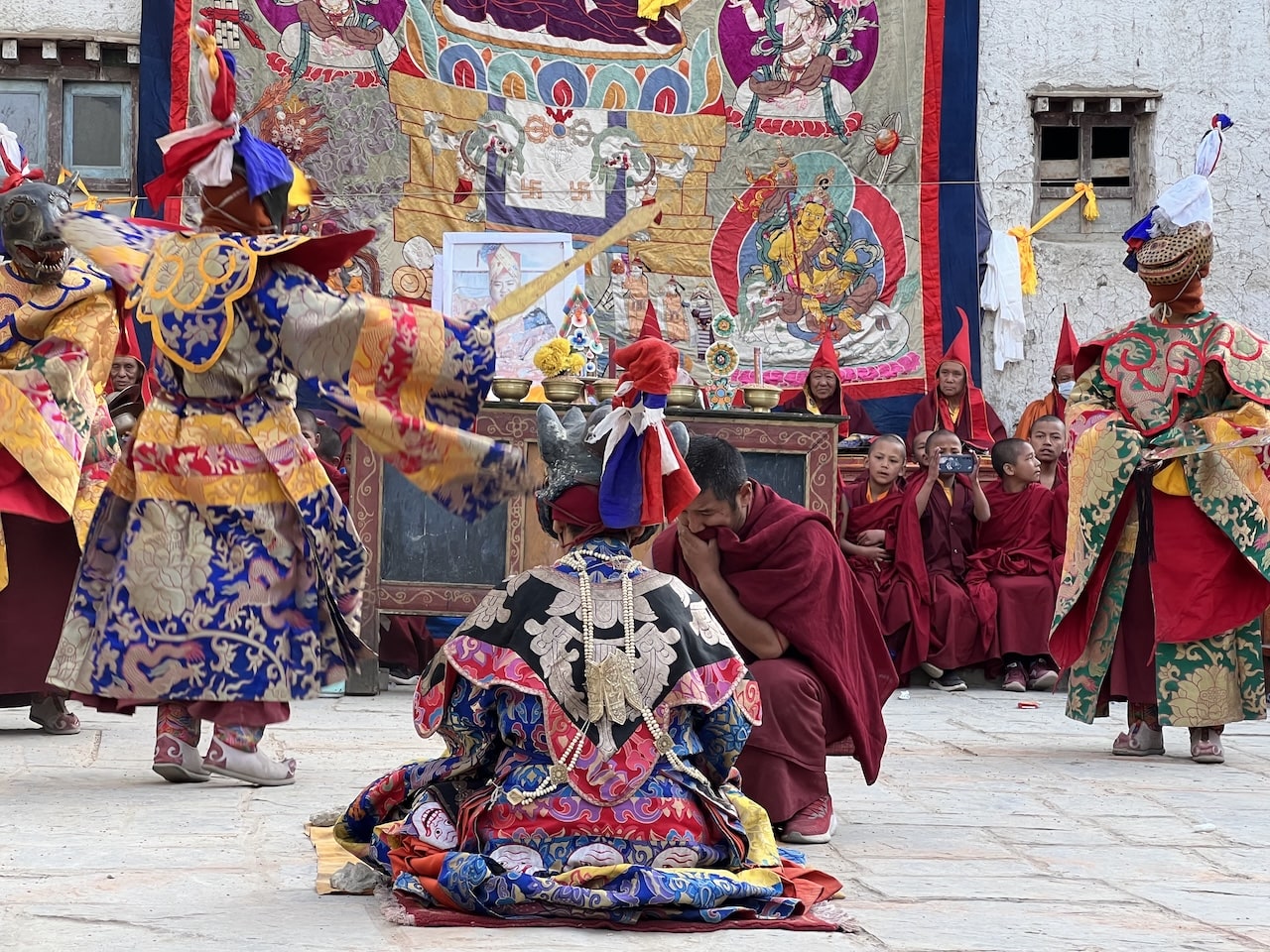 Tiji Festival Danzatori mascherati in costumi tradizionali colorati e monaci in tuniche rosse durante una cerimonia rituale.