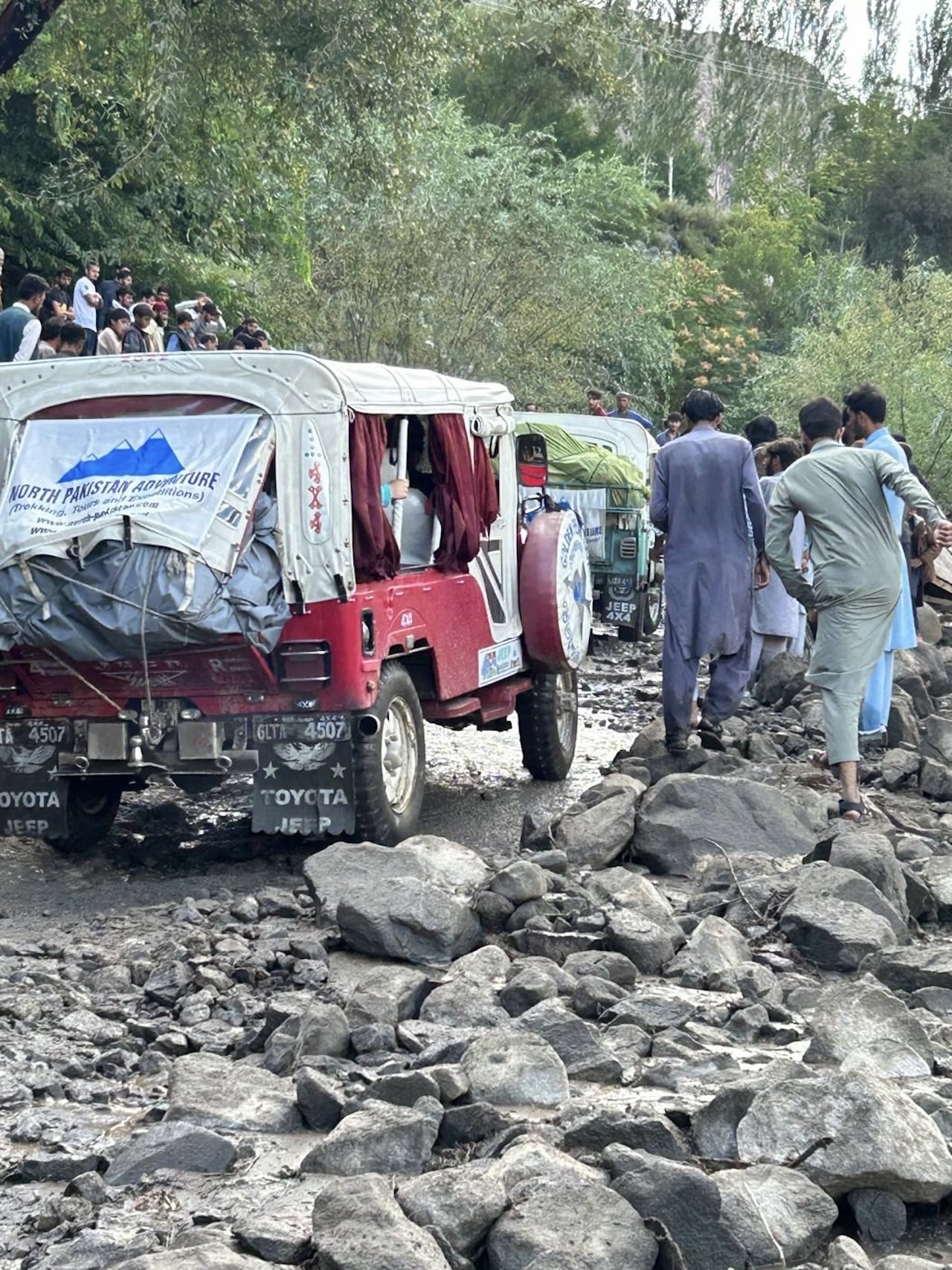 Jeep 4x4 rosse e verdi bloccate su una strada di montagna molto rocciosa in Pakistan; un gruppo di uomini cammina