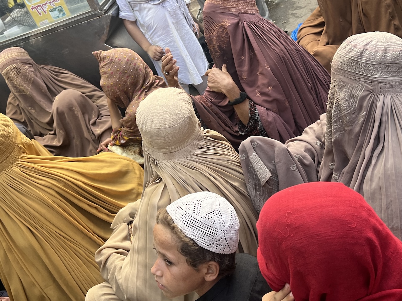 Folla a Peshawar Primo piano di un bambino con un cappello lavorato a maglia tra donne con burqa color terra in una folla a Peshawar.
