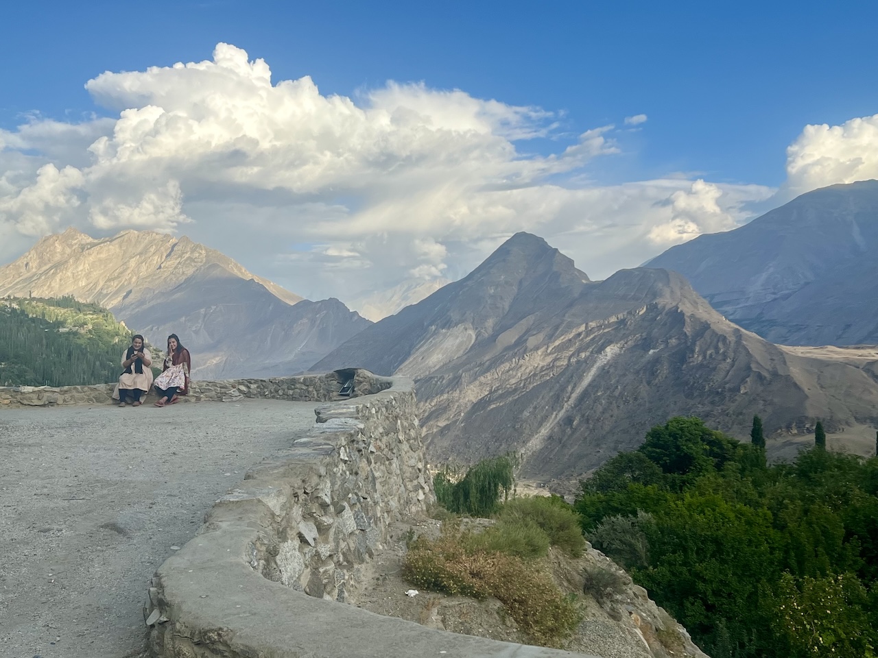 Veduta panoramica di Karimabad nella Valle di Hunza: due donne sedute su un muro con maestose montagne sullo sfondo