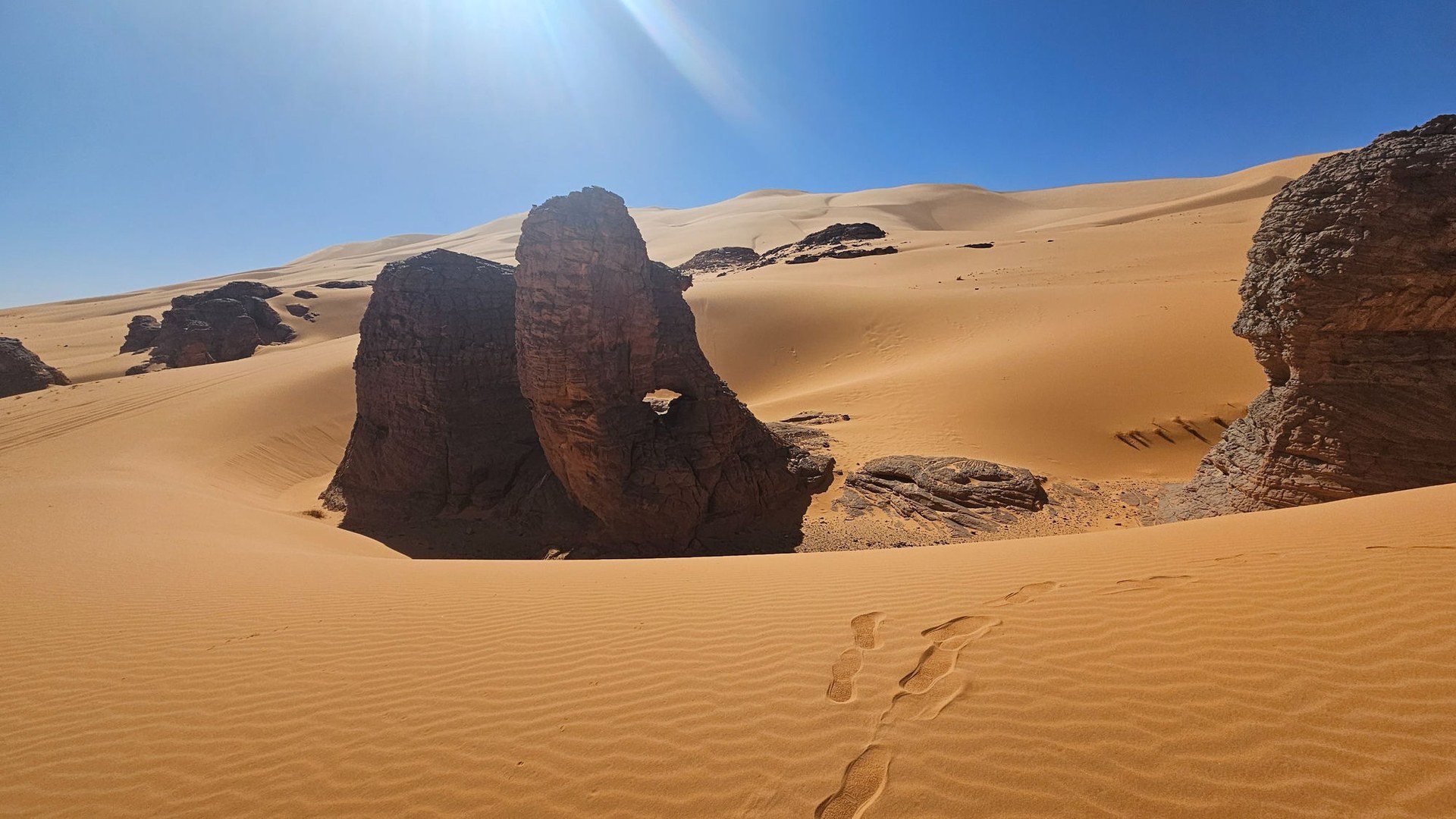 Formazione rocciosa scolpita dal vento tra le dune del deserto del Sahara algerino, con impronte sulla sabbia