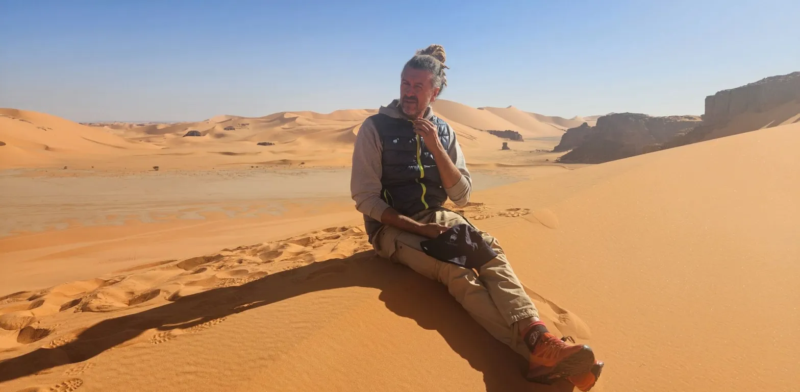 Viaggiatore seduto su una duna durante un tour nel deserto dell'Algeria, sullo sfondo le dune del Tassili n'Ajjer