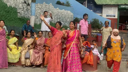 Gruppo di donne in sari colorati sorride e saluta per strada a Pokhara, con uomini e bambini sullo sfondo