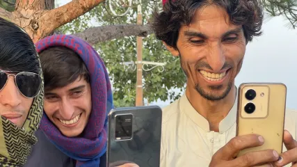Tre uomini sorridenti, uno con cappello rosso, che guardano i loro smartphone all'aperto