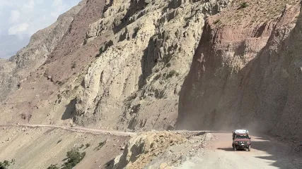 Veicolo 4x4 rosso che percorre una stretta strada sterrata e polverosa tra ripide pareti rocciose di montagna