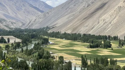 Ampia valle verde con campi agricoli, alberi, un fiume e ripidi pendii montuosi e aridi